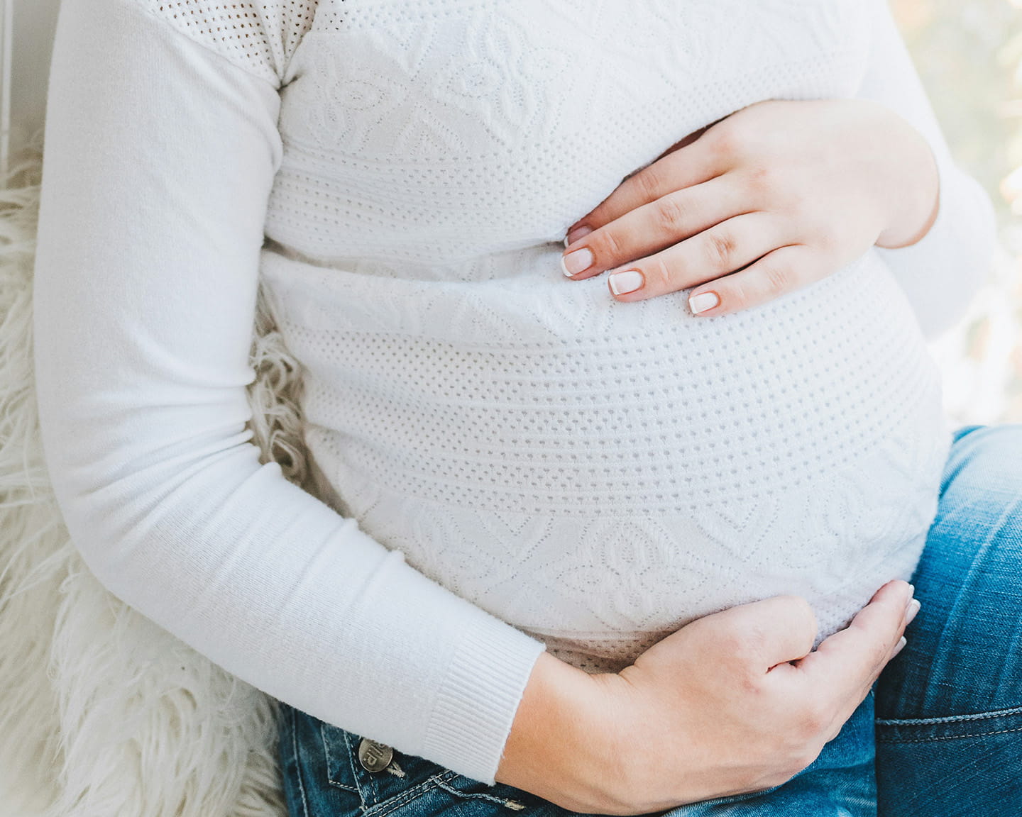 Donna incinta vestita di bianco che abbraccia il pancione
